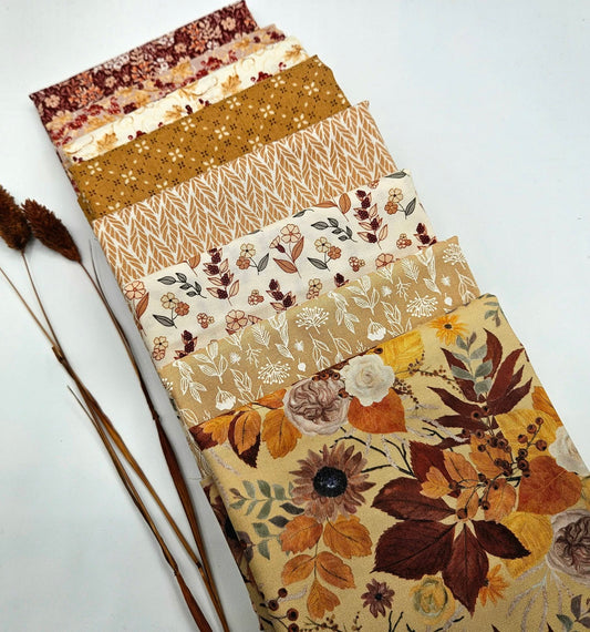 An 8-piece stack of Riley Blake Evening on the Prairie fabric cuts fanned out diagonally. The bundle features warm autumn colors including mustard yellow, burgundy, rust terracotta, and cream cotton quilting fabrics with floral, leaf, herringbone, and geometric prints.