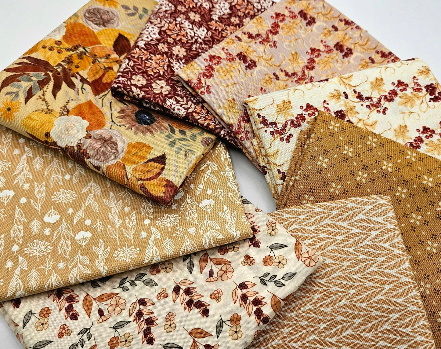 A top-down view of an 8-piece fall fabric bundle by Modern Prairie for Riley Blake arranged in a circular swirl. Displays coordinating 100% cotton quilting fabrics in rich burgundy, harvest gold, and ivory cream with ditsy floral and botanical vine patterns.