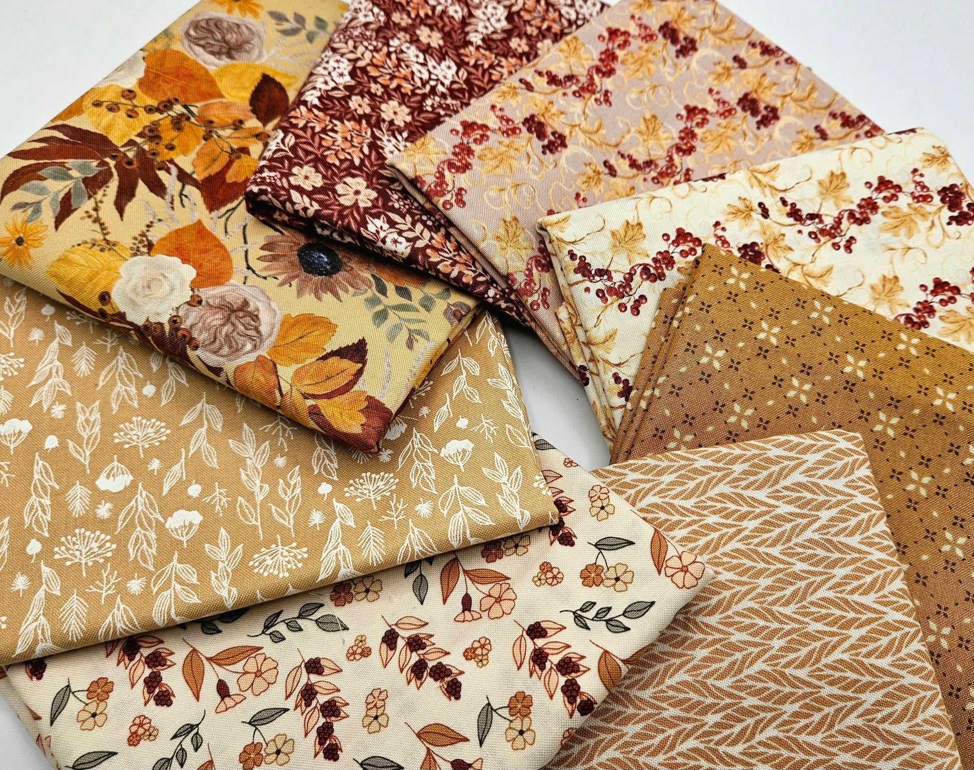 A top-down view of an 8-piece fall fabric bundle by Modern Prairie for Riley Blake arranged in a circular swirl. Displays coordinating 100% cotton quilting fabrics in rich burgundy, harvest gold, and ivory cream with ditsy floral and botanical vine patterns.