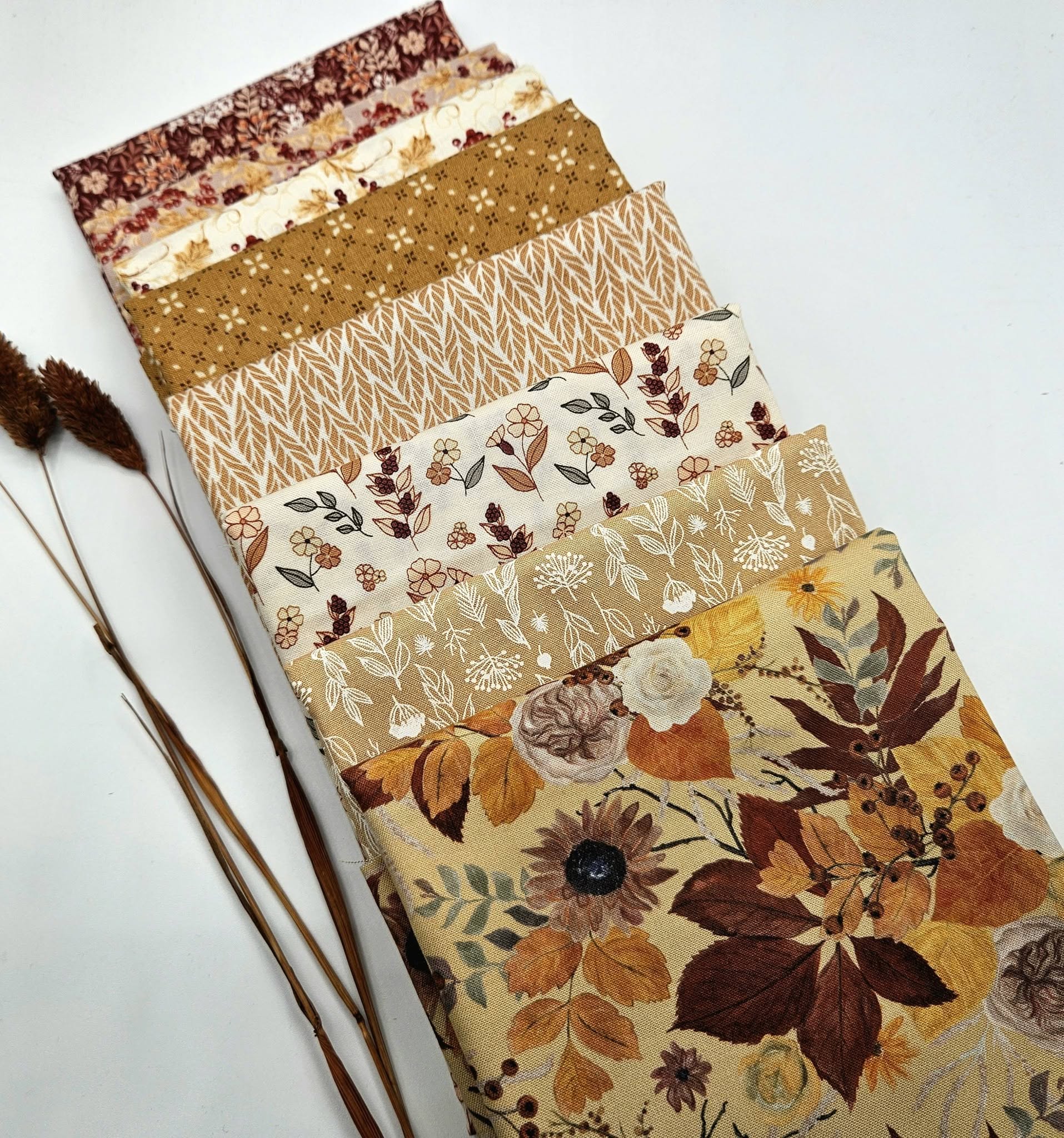 An 8-piece stack of Riley Blake Evening on the Prairie fabric cuts fanned out diagonally. The bundle features warm autumn colors including mustard yellow, burgundy, rust terracotta, and cream cotton quilting fabrics with floral, leaf, herringbone, and geometric prints.